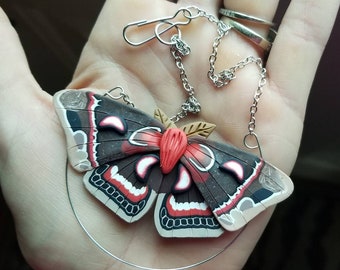 May include: A silver chain necklace with a red, white, and black butterfly pendant. The butterfly has a detailed design and is made of polymer clay.