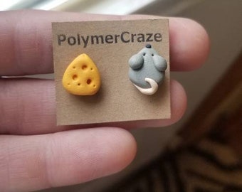 May include: A pair of polymer clay earrings, one shaped like a wedge of cheese and the other shaped like a mouse. The earrings are displayed on a card with the text "PolymerCraze".