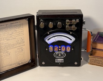 May include: A vintage Weston A.C. & D.C. Ammeter Model 370. The black meter has a glowing blue display showing "12:00". The open wooden case reveals a document. A stack of books is to the right.