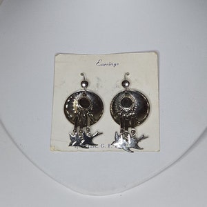 May include: Silver tone earrings with a round disc and dangling birds. The earrings are on a white card with the word "Earrings" printed on it.