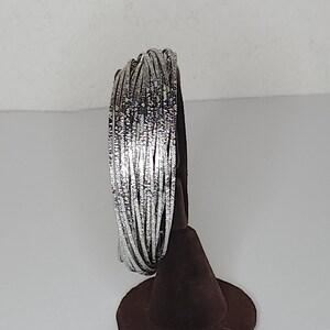 May include: A stack of silver bangles with a textured finish. The bangles are displayed on a brown velvet stand.