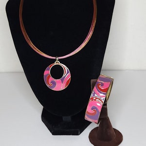 May include: A gold necklace with a pink and purple enamel pendant and a matching bracelet. The pendant is a circle with a swirl design. The bracelet is a bangle with a similar swirl design.