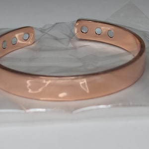 May include: A rose gold colored copper bracelet with five silver magnetic dots on the top. The bracelet is in a clear plastic bag.