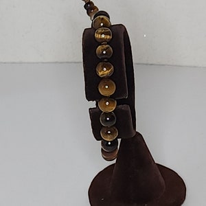 May include: A brown leather bracelet with tiger's eye beads. The bracelet is displayed on a brown velvet stand.