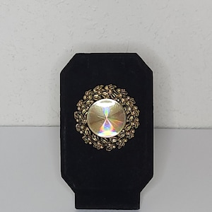 May include: A gold-toned brooch with a round iridescent glass stone surrounded by a floral design.