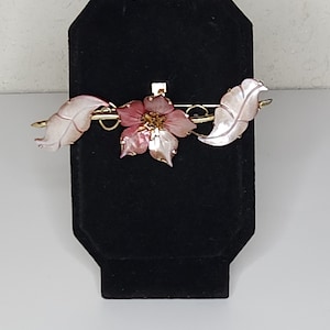 May include: A pink flower with gold accents and two white leaves, all made of shell, are attached to a gold bar pin.
