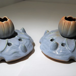 May include: Two blue and brown ceramic flower bud vases with a leaf design. Each vase has a small opening at the top and several small holes around the base.