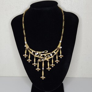 May include: A gold-tone necklace with a delicate chain and a dangling pendant featuring a cluster of small flowers and clear rhinestones.