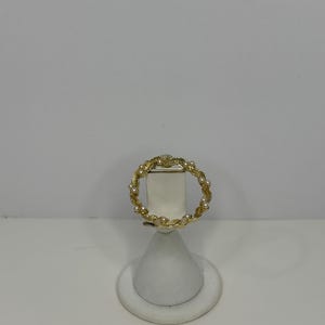 May include: A gold ring with a twisted design and small white pearls. The ring is on a white display stand.