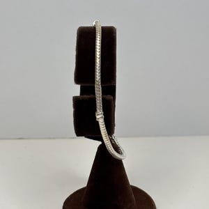 Peut inclure: Un bracelet en chaîne de serpent argenté sur un présentoir en velours brun.