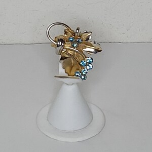 May include: A gold and silver ring featuring a leaf design and blue gemstones. The ring is displayed on a white stand.