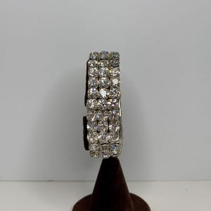 Peut inclure: Un bracelet argenté avec trois rangées de strass transparents.