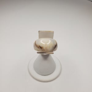 May include: A white ring with brown marbling on a white ring stand.