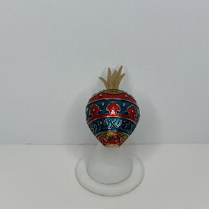 May include: A gold-tone ring with a red, blue, and gold enamel design. The ring is shaped like a heart with a small, gold-tone spike on top.