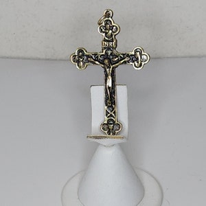 Op de afbeelding: Een gouden crucifix-hanger met een zwart geverfd figuur van Jezus Christus. Het crucifix heeft ingewikkelde details en een "INRI" inscriptie.
