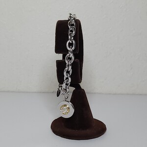 Pode incluir: Um bracelete de corrente de prata com um fecho redondo que apresenta um grupo de pequenas pedras transparentes.