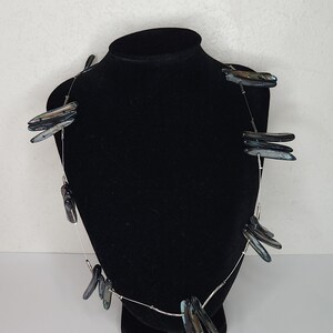 Peut inclure: Un collier en chaîne argent avec plusieurs pendentifs en coquille nacrée noire et bleue. Le collier est présenté sur un buste de mannequin en velours noir.