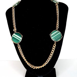 May include: A gold chain necklace with four large green and white oval-shaped stones. The necklace is displayed on a black velvet mannequin.