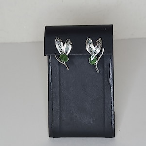 Puede incluir: Un par de pendientes de plata con detalles de piedras preciosas verdes. Los pendientes tienen forma de mariposa estilizada con alas delicadas.