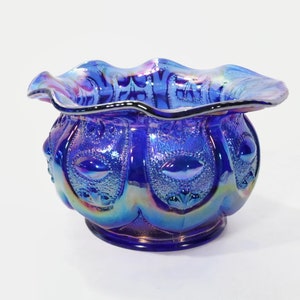 Puede incluir: Un cuenco de vidrio azul iridiscente con un borde festoneado y un patrón decorativo. El cuenco tiene un acabado nacarado y es perfecto para servir aperitivos o postres.