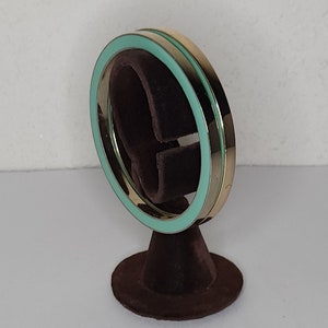 May include: A pair of gold bangle bracelets with a turquoise enamel trim. The bracelets are displayed on a brown velvet stand.