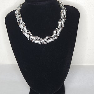 May include: A silver chain necklace with a twisted design. The necklace is displayed on a black velvet bust form.