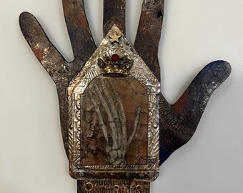 Könnte beinhalten: Eine wandmontierte, handförmige Plakette mit dunklem, abgenutztem Finish. In der Mitte befindet sich ein metallischer Schrein mit einer Skeletthand-Illustration, gekrönt von einer kleinen Krone und einem Stern. Darunter hängen ein Kreuz und ein geflügelter Orb.