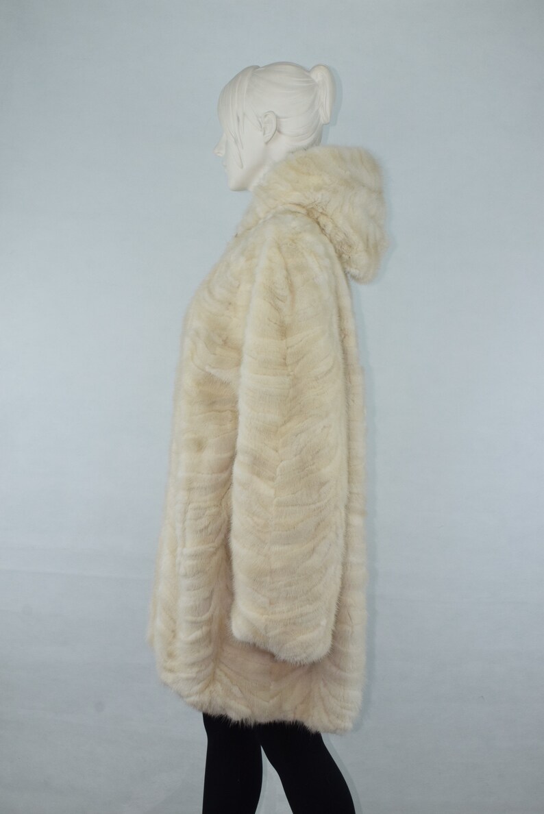May include: A white fur coat with a hood. The coat is made of a soft, fluffy fur and has a long, flowing style.