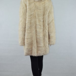 May include: A white fur coat with a hood. The coat is made of a soft, fluffy fur and has a long, flowing style. The coat is being worn by a mannequin.