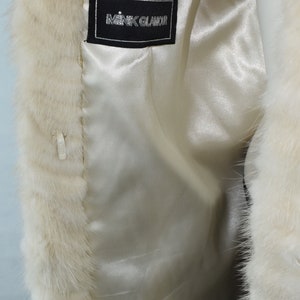 May include: White fur coat with a black label that reads "Mink Glamoor" on the inside lining.