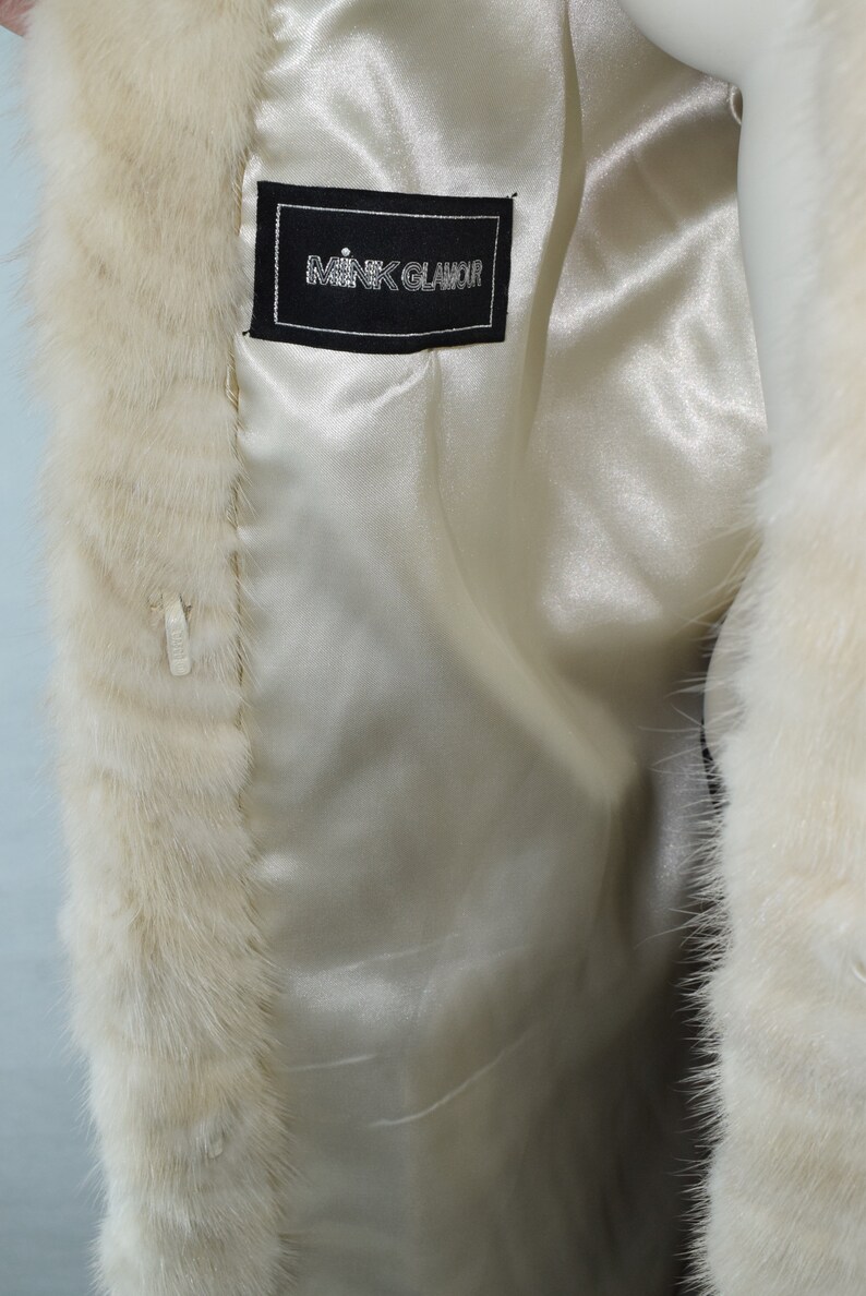 May include: White fur coat with a black label that reads "Mink Glamoor" on the inside lining.