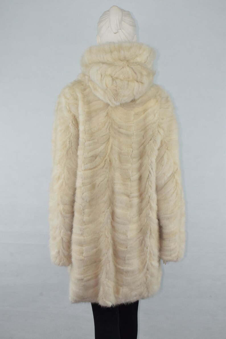May include: A cream-colored fur coat with a hood. The coat is made of a soft, plush fur and has a long, flowing style.