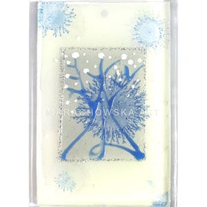 Könnte beinhalten: Ein quadratischer, transparenter Glasanhänger mit weißem Hintergrund und einem blauen und weißen Schneeflockenmuster. Die Schneeflocke ist von einem silbernen Rahmen umgeben und es sind kleinere Schneeflocken um den Anhänger herum verstreut. Der Text "MARACHOWSKA ART" ist am unteren Rand des Anhängers sichtbar.