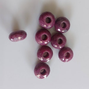 Peut inclure: Dix perles de rubis rouge facettées avec un trou au centre. Les perles sont disposées en un groupe lâche sur une surface blanche.