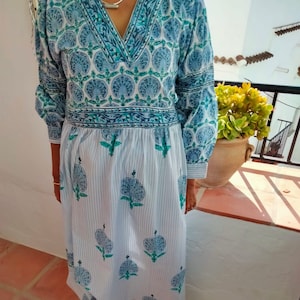 May include: A long, white dress with blue and green floral print. The dress has a V-neckline and a gathered waist. The skirt is striped and has a flowing silhouette.