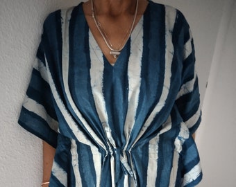 Puede incluir: Vestido kaftán a rayas azules y blancas, con cuello en V y cintura ajustable con cordón. El vestido tiene mangas cortas y un corte holgado. La tela parece ligera, ideal para climas cálidos.