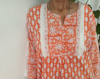 Puede incluir: Una túnica naranja de manga larga con un estampado de peces blancos y un borde floral. La túnica tiene cuello en V y un corte holgado.