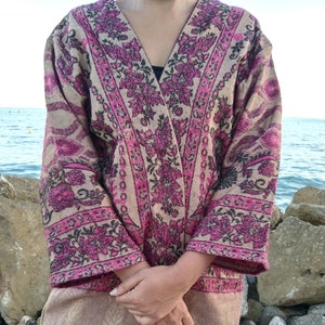 May include: A long-sleeved, pink and beige patterned cardigan with a V-neck. The cardigan has a floral design with black accents.