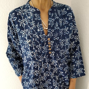Puede incluir: Un vestido de manga larga azul y blanco con estampado, cuello en V y cierre de botones. El vestido tiene un frente plisado y un ajuste holgado.