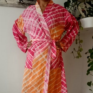 May include: A pink and orange tie-dye robe with a long sleeve and a sash tie.