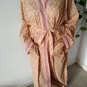 Może przedstawiać: Żółta i różowa bawełniana szlafrok z kwiatowym nadrukiem, długimi rękawami i paskiem do wiązania.