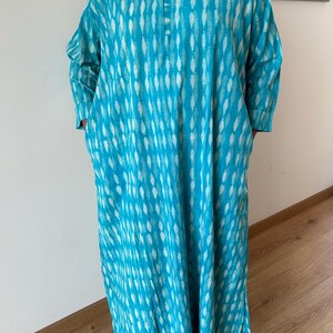 May include: A long, turquoise blue dress with a white and turquoise pattern. The dress has a round neckline and long sleeves.