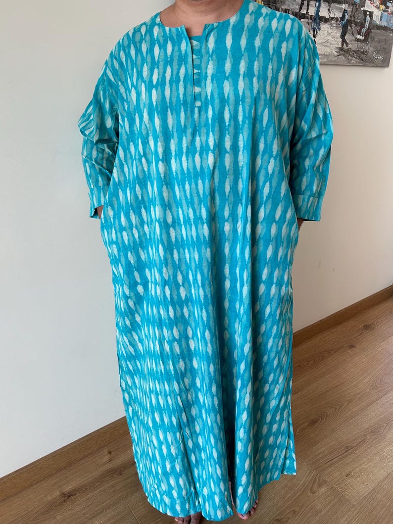 May include: A long, turquoise blue dress with a white and turquoise pattern. The dress has a round neckline and long sleeves.