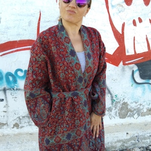 May include: A long, red, blue, and green patterned robe with a sash tie. The robe has a paisley design and is worn by a person wearing sunglasses.