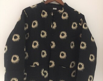Pode incluir: Uma jaqueta acolchoada preta com um padrão circular branco e preto. A jaqueta tem um colar mandarim e um fecho de botão.