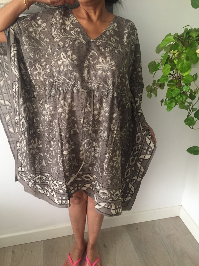 May include: A gray and white floral print kaftan with a V-neck and a tie at the waist.