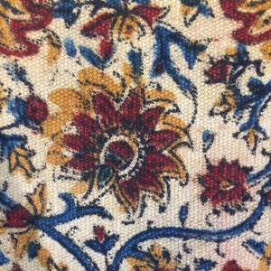 May include: Close-up of a fabric with a floral pattern. The fabric is white with blue, red, and yellow flowers. The flowers are intricate and detailed.