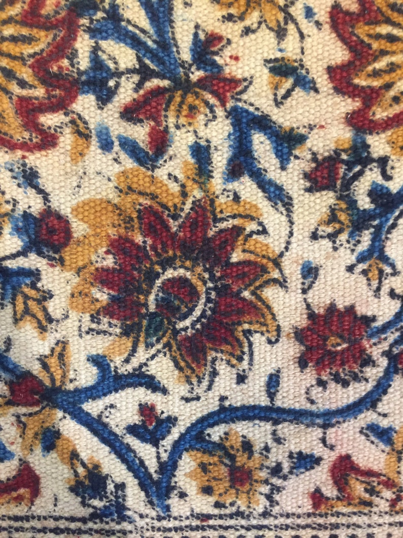May include: Close-up of a fabric with a floral pattern. The fabric is white with blue, red, and yellow flowers. The flowers are intricate and detailed.