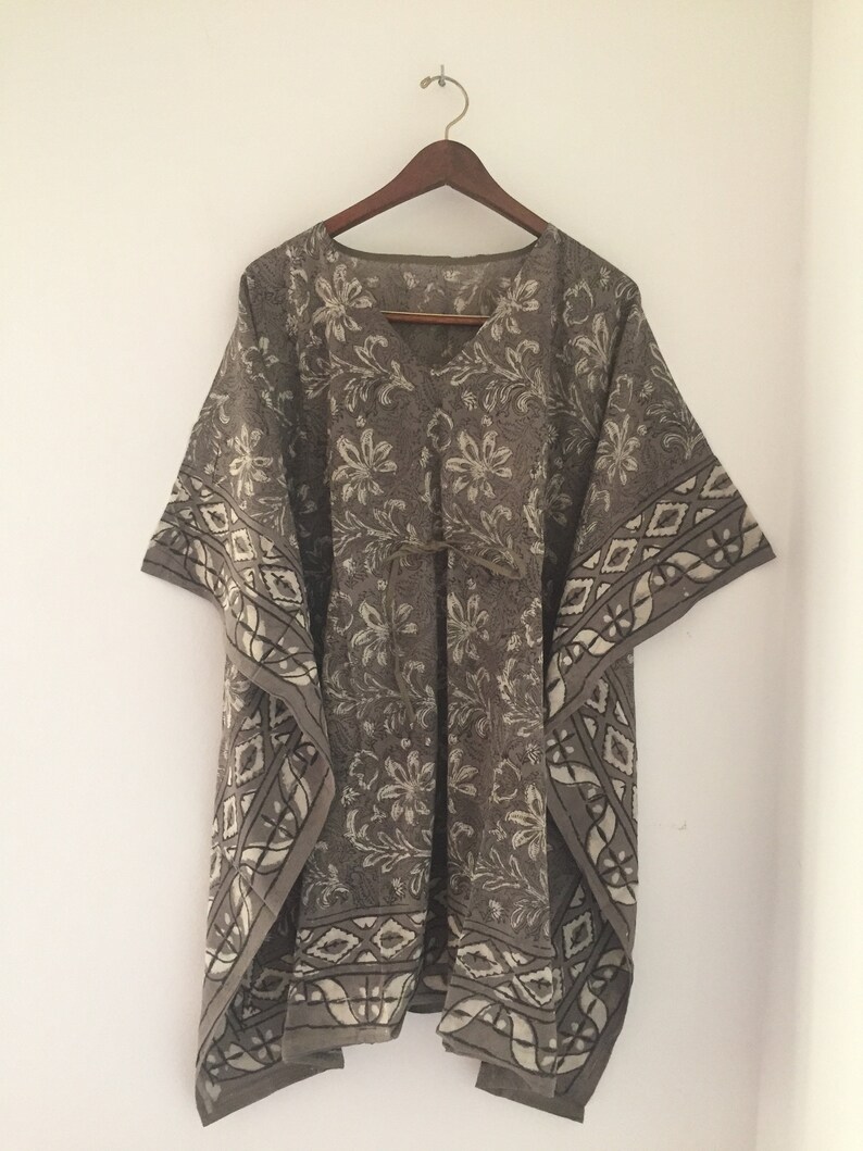 May include: A brown and white patterned cotton kaftan with a V-neck and short sleeves. The kaftan has a tie at the waist and a geometric pattern around the hem.