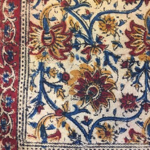 May include: A close-up of a fabric with a floral pattern. The fabric is white with blue, red, and yellow flowers. The fabric has a border of red and blue.